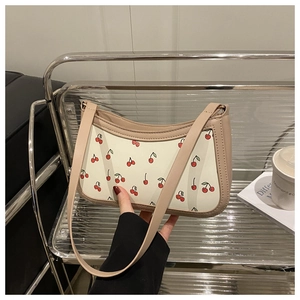 Close-up of stylish off-white shoulder bag featuring red cherry prints and leather strap