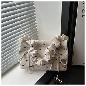 Detail of white canvas cloud bag featuring vintage red ribbon patterns and pleated strap