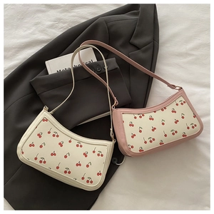 Detail of trendy cherry print hobo shoulder bags in cream and pink on a stylish bed setting