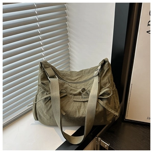 Detail of army green nylon tote bag featuring bow drawstrings and wide strap on windowsill