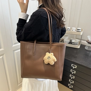 Brown leather tote bag with star plush charm shown from the side in home setting