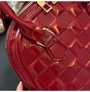 Detail of red patent leather shell bag featuring geometric embossed pattern and gold hardware