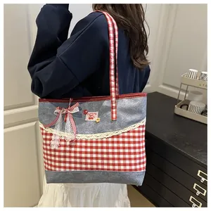Close-up of red plaid denim tote bag featuring white lace trim and cherry logo detail