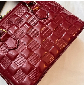 Macro detail of red glossy patent leather shell bag with textured checkered pattern and gold hardware