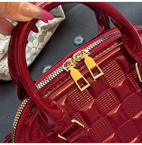 Close-up of glossy red patent leather shell bag with quilted square texture and gold zipper
