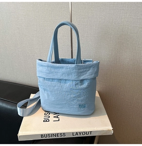 Détail du sac seau en toile bleu clair avec texture plissée et broderie de la marque