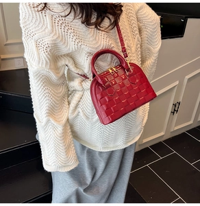 Detail of red quilted patent leather shell bag with gold hardware worn as crossbody