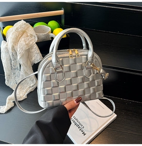 Detail view of silver shell-shaped handbag with embossed grid pattern and gold zippers