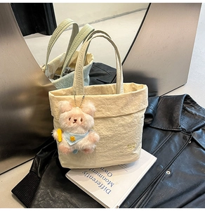 Détail du sac cabas beige avec texture de papier froissé et un pendentif ours en peluche