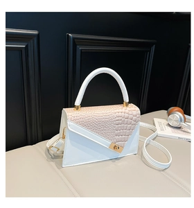 Detail der weiß-beigen Handtasche mit Krokodilprägung und goldenem Drehverschluss