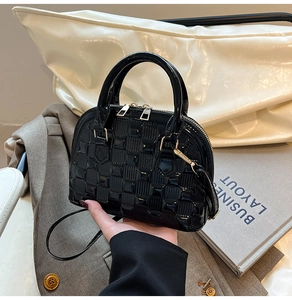 Detail of black patent leather shell bag with textured checkered pattern and gold zippers