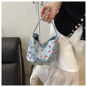 Detail of light blue tote bag with red cherry prints held by a model in a casual setting