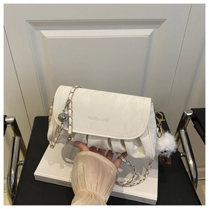 Macro detail of white pleated shoulder bag featuring a silver chain strap and furry charm