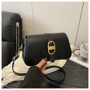 Detail of black leather shoulder bag featuring a large gold oval buckle with woven texture