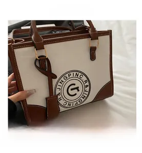 Close-up of canvas tote bag showing brown leather trim and circular letter logo detail