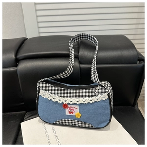 Detail of blue denim shoulder bag with checkered trim, white lace, and cherry patch