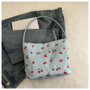 Detail view of large cherry print shoulder bag on blue denim jacket and fabric
