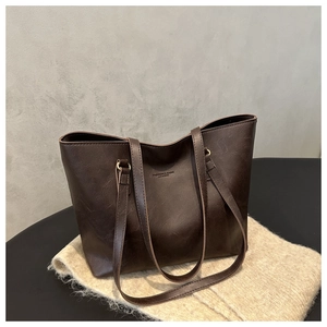 Dettaglio della borsa tote in pelle marrone vintage con scritte in rilievo su maglia morbida