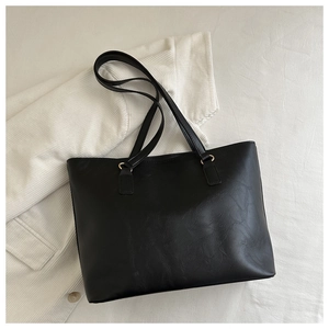 Dettaglio borsa tote in pelle PU nera con lunghi manici su sfondo in velluto a coste bianco