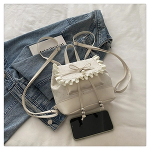 Detail of cream mini backpack with ruffle trim, bow, and pearl on white fabric
