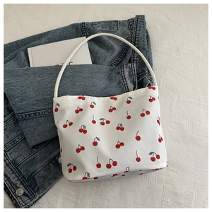 Detail of white cherry print handbag on bed showing canvas texture and slender handle