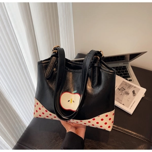 Close-up of cute apple pattern and red polka dots detail on black leather tote bag