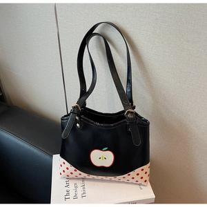 Detail view of black tote bag with red apple print and polka dot pattern on a book