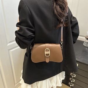 Brown leather crossbody bag with oval gold buckle, worn by model in stylish outfit