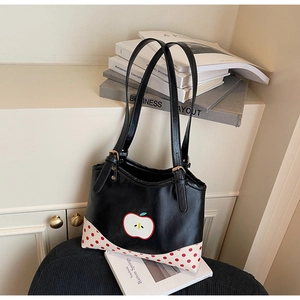 Detail of a black leather tote featuring a cartoon apple patch and red polka dot corners