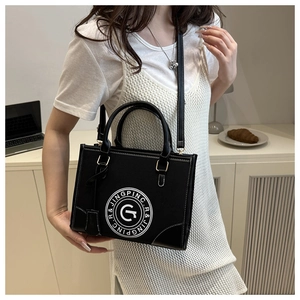 Detail of black faux leather tote bag with round white logo and gold hardware on a model