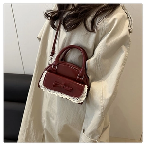 Detail of burgundy patent leather mini bag with lace trim shown on a model