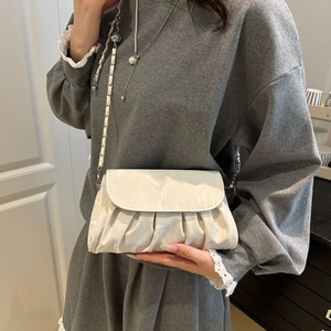White ruched cloud crossbody bag with metallic chain strap worn by a model in casual grey suit