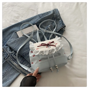 Macro shot of light blue mini backpack with white lace trim and red bow embroidery
