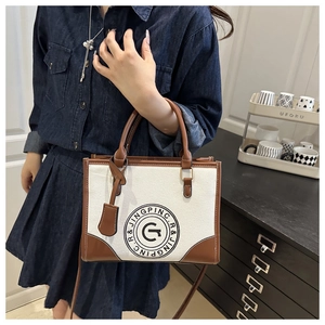 Detail of canvas tote bag with brown leather trim and circular letter logo embroidery