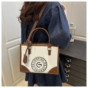 Close-up of retro canvas tote bag featuring leather stitching and circular letter logo