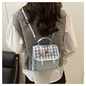 Detail of light blue plaid backpack with apple logo worn by a model in casual outfit