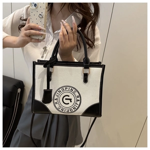 Detail of canvas and black leather tote bag with circular printed logo and metal hardware
