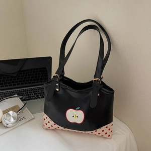 Black tote bag with apple illustration and red polka dot details on a desk setting