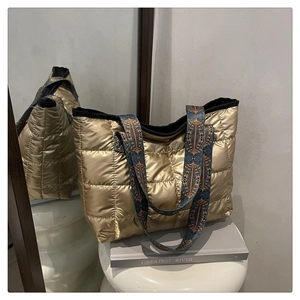 Dettaglio di una borsa tote dorata trapuntata con tracolla larga a motivo etnico