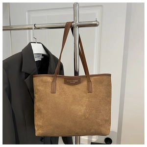 Close-up of brown suede tote bag with leather handles and embossed brand lettering detail