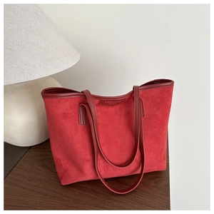 Détail du cabas en daim rouge avec logo embossé sur les finitions en cuir premium