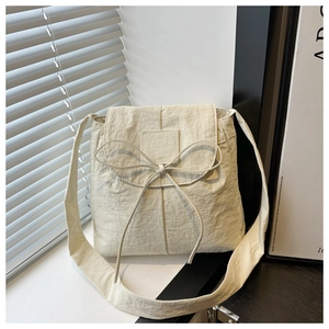Close-up of cream square bag with ribbon bow and pleated fabric under shadow lighting