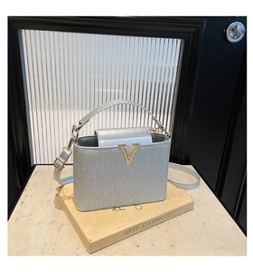Detail of silver glitter box handbag with gold V-clasp on an artistic book stand