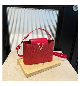 Detailed shot of red glitter tote bag with golden V-logo on ivory book backdrop