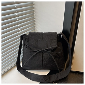 Detail of a black nylon crossbody bag featuring a decorative bow and pleated texture