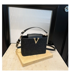 Detail of sequin bucket bag with golden V-logo hardware on stylish black glitter surface