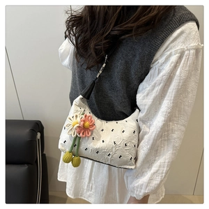 Detail of white quilted crossbody bag with floral charm and black K-pattern embroidery