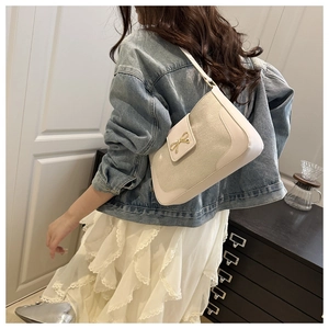 Detail of cream leather shoulder bag with gold bow clasp on a model in denim and lace