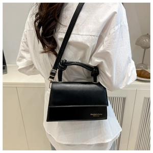 Detail of black leather crossbody bag featuring a knotted handle and gold printed text