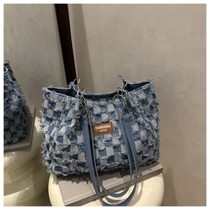 Close-up of blue checkered denim tote bag with fringed edges and leather brand tag